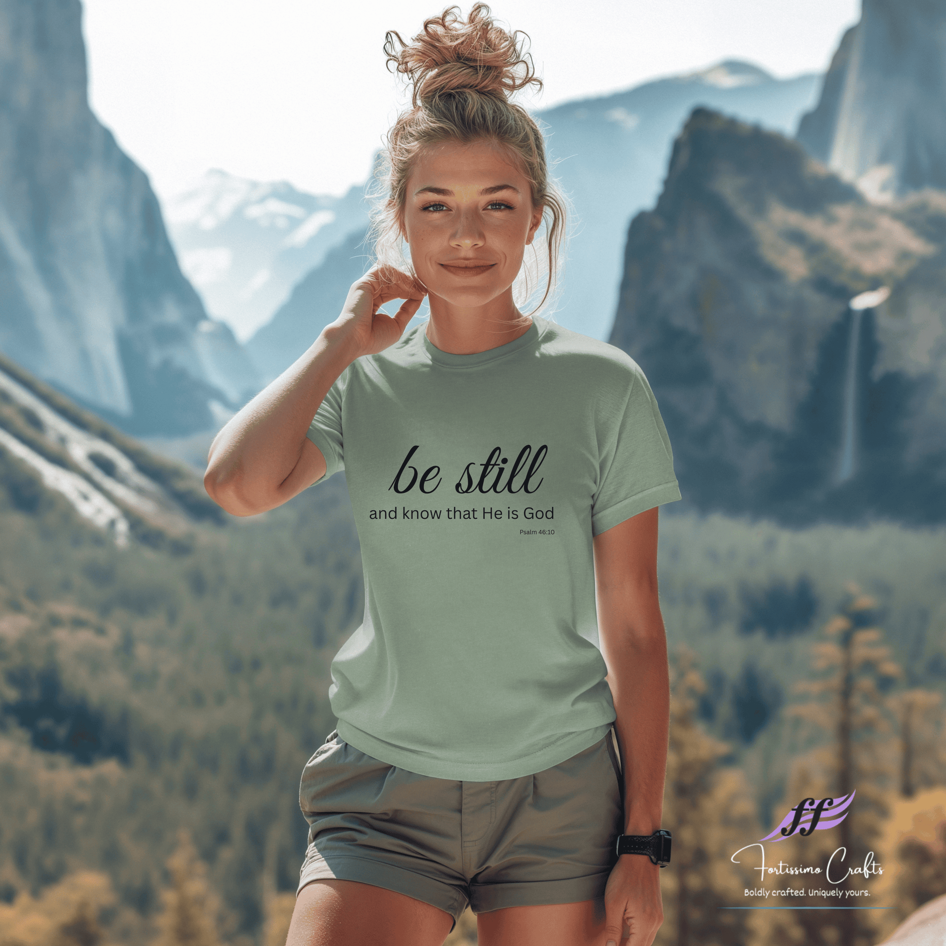 Woman wearing a t-shirt with 'be still and know that He is God' in a mountainous landscape