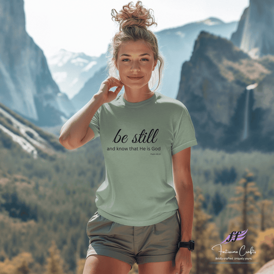 Woman wearing a t-shirt with 'be still and know that He is God' in a mountainous landscape