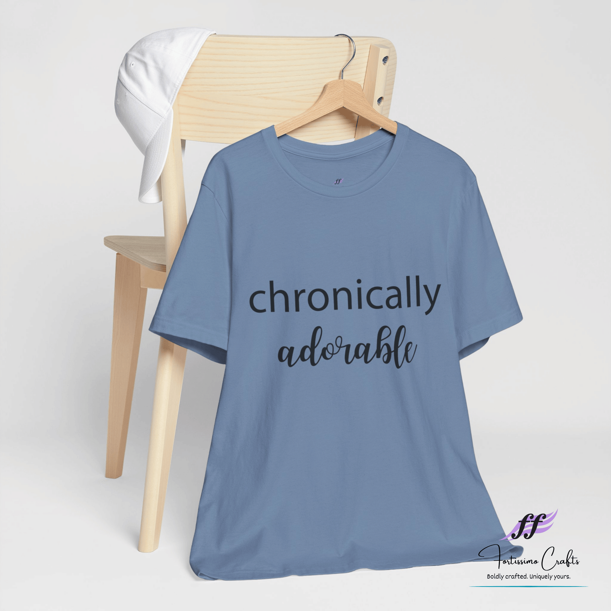Blue t-shirt with 'chronically adorable' text on a wooden chair against a white background