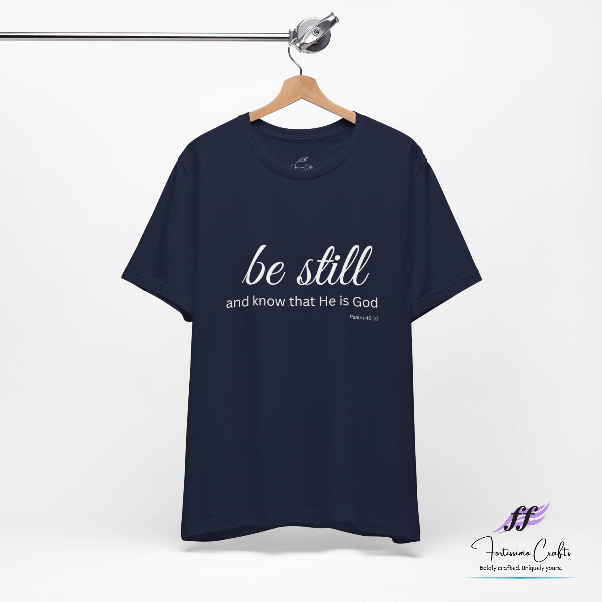 Navy blue t-shirt with 'be still and know that He is God' text on a hanger against a white background.