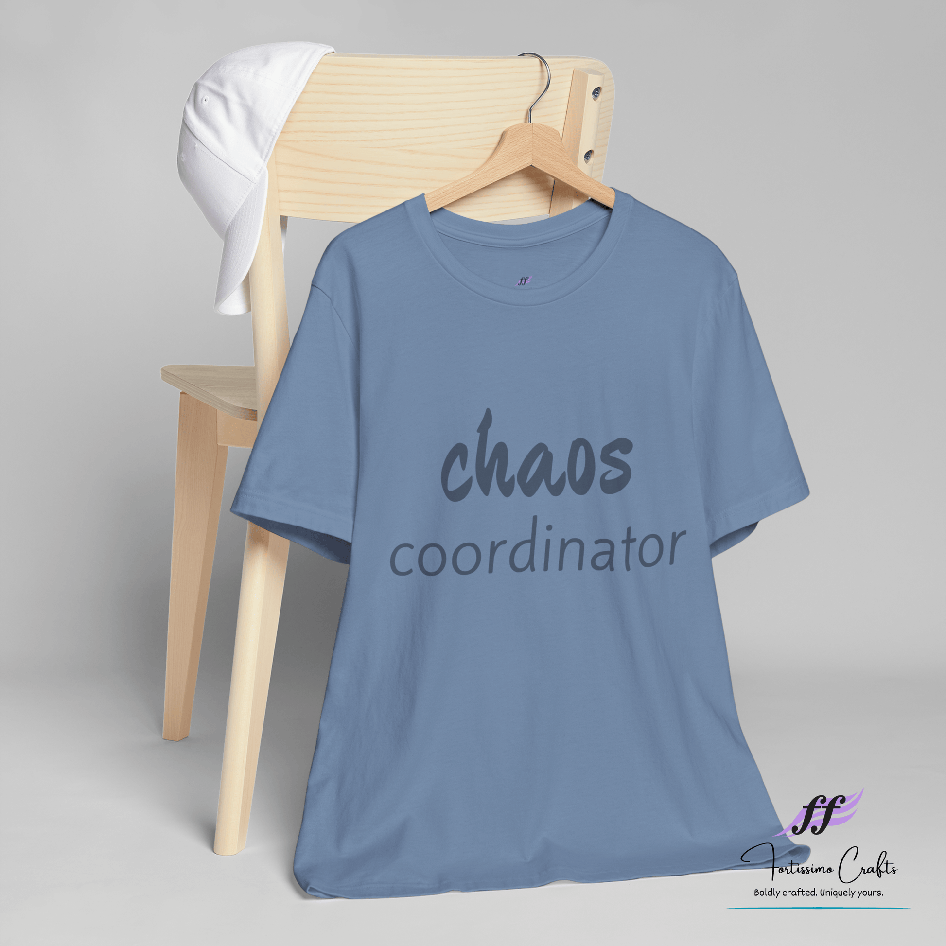 Blue t-shirt with 'chaos coordinator' text on a wooden chair against a gray background