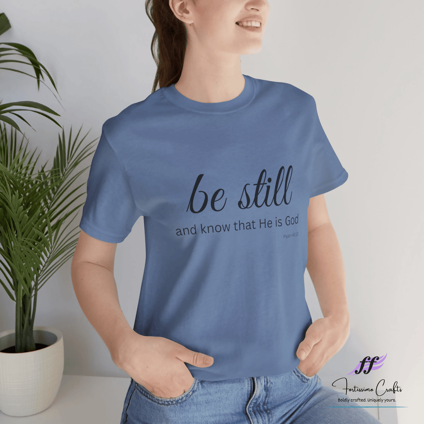 Person wearing a blue t-shirt with 'be still and know that He is God' text, standing indoors.