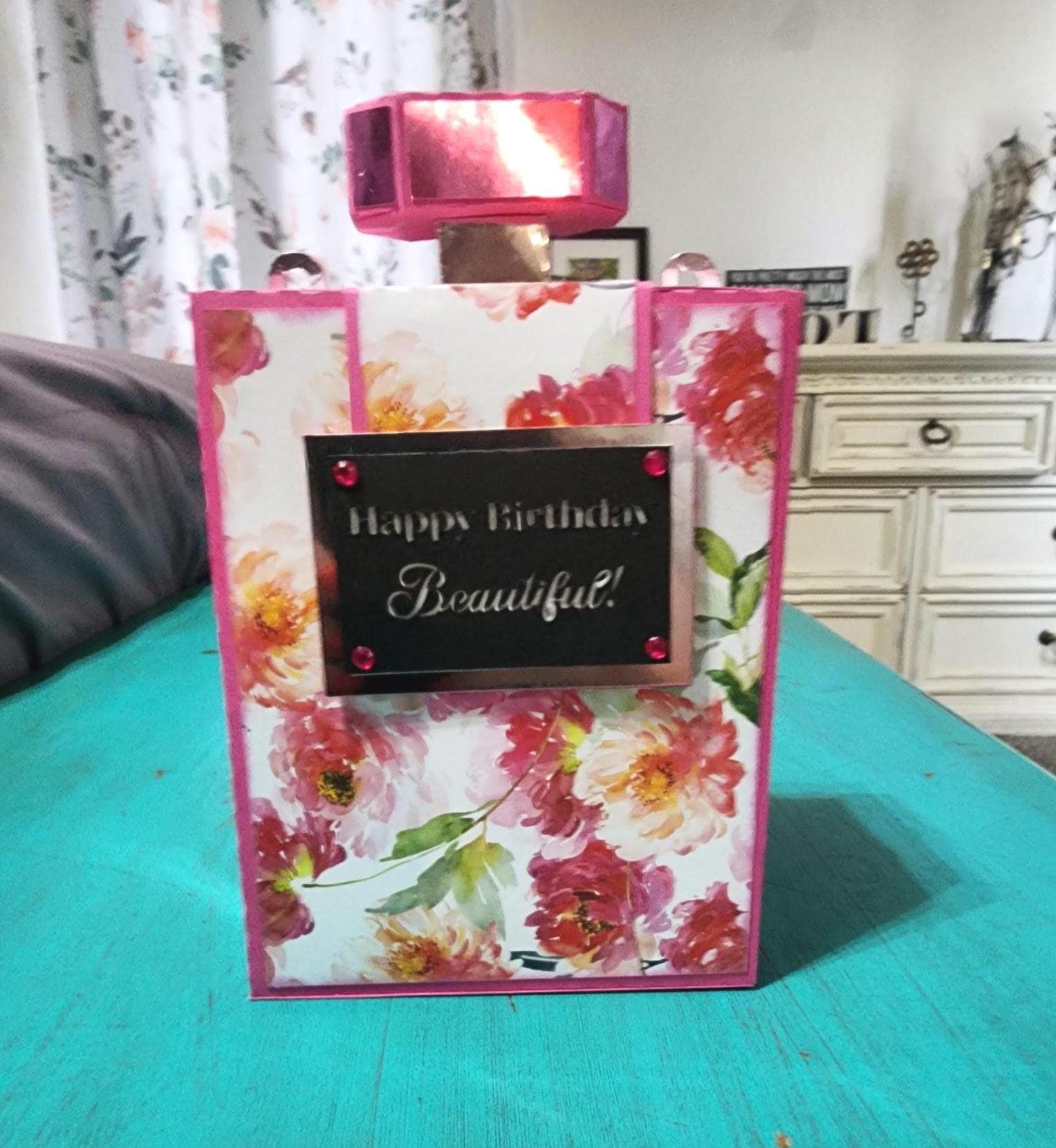 Floral-patterned gift box with 'Happy Birthday Beautiful' card on a teal surface.