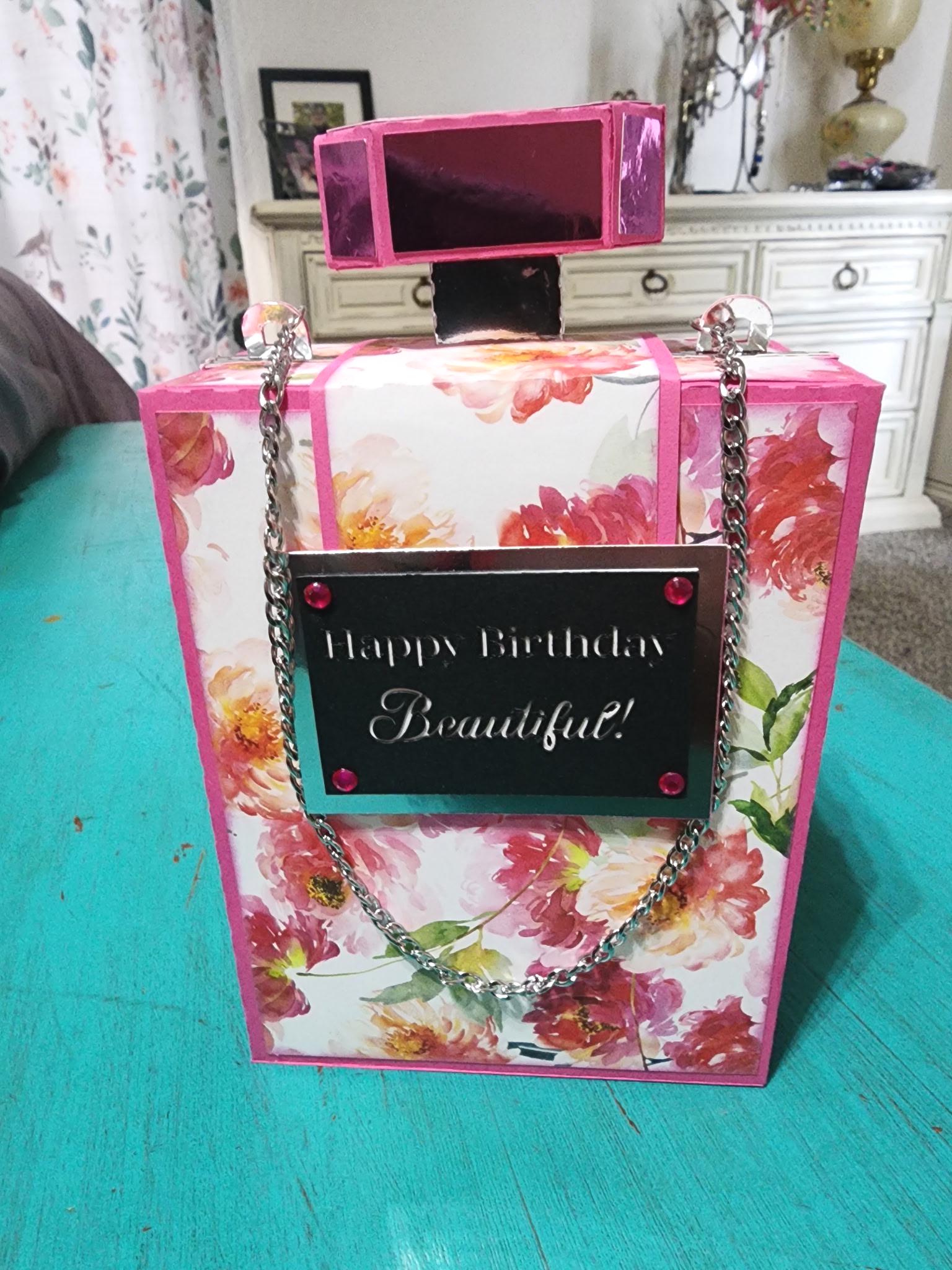 Floral gift bag with 'Happy Birthday Beautiful!' message on a teal surface