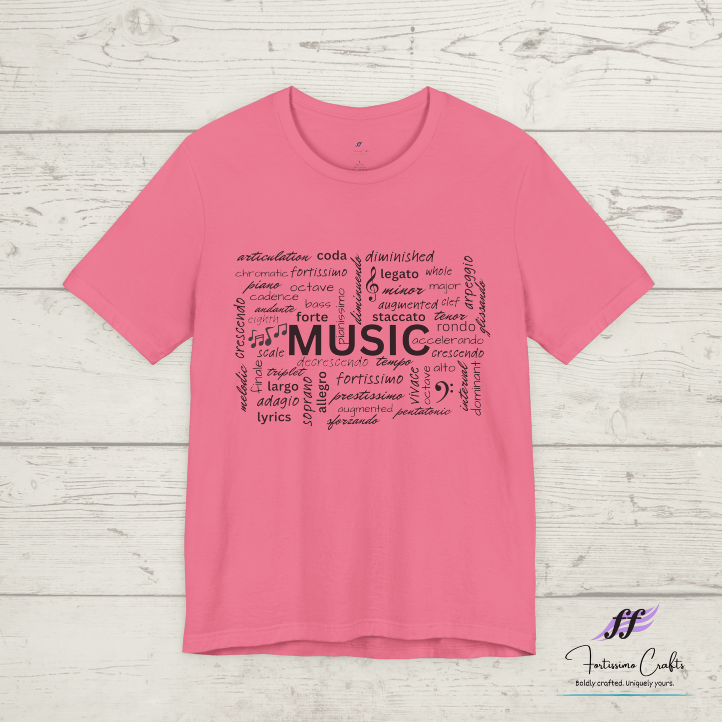 Pink t-shirt with black music-themed text design on a wooden surface