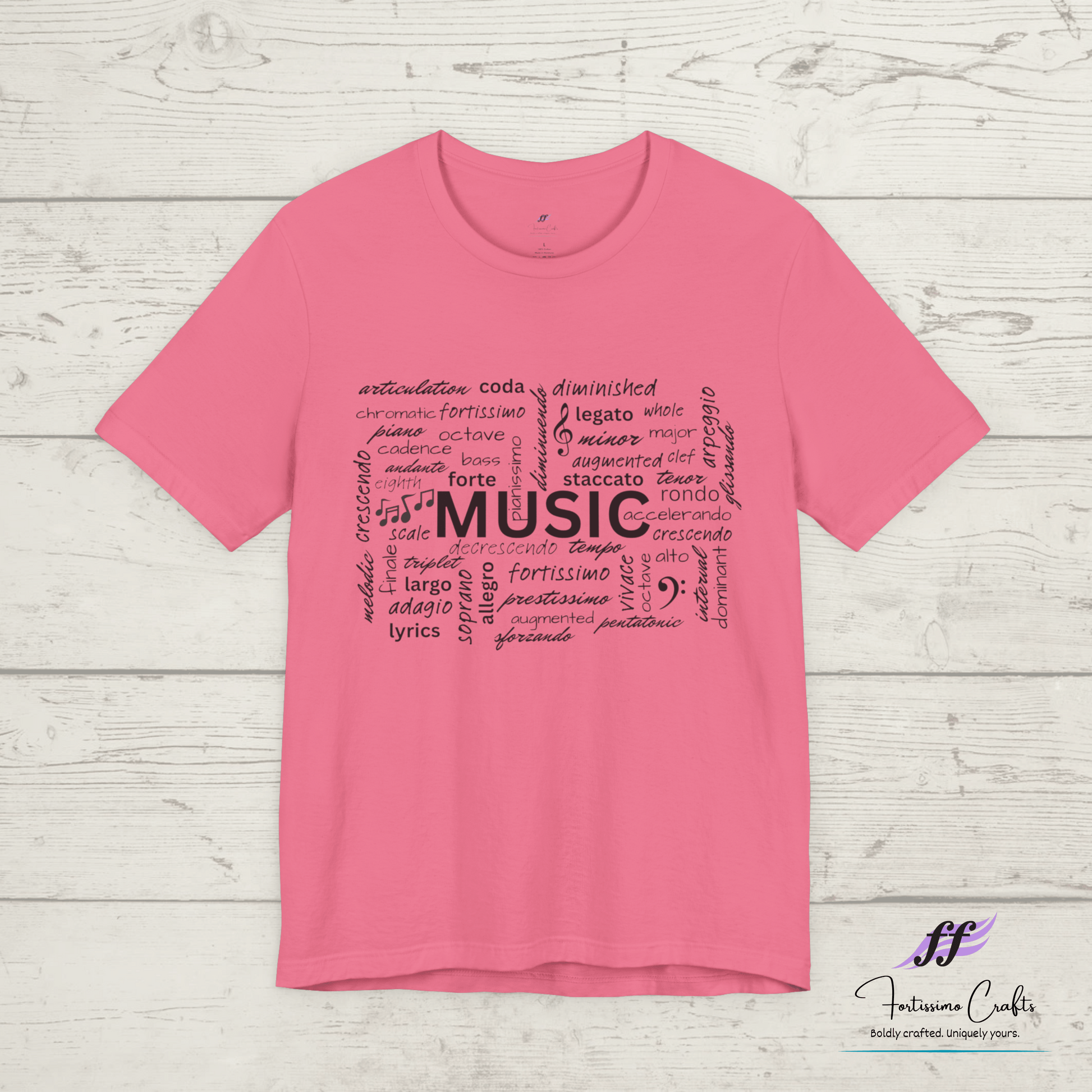 Pink t-shirt with black music-themed text design on a wooden surface