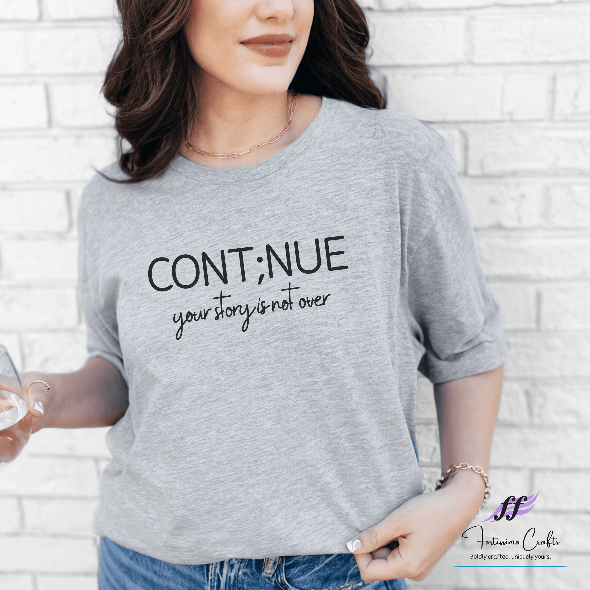 Person wearing a gray t-shirt with 'CONTINUE your story is not over' text against a white brick wall.