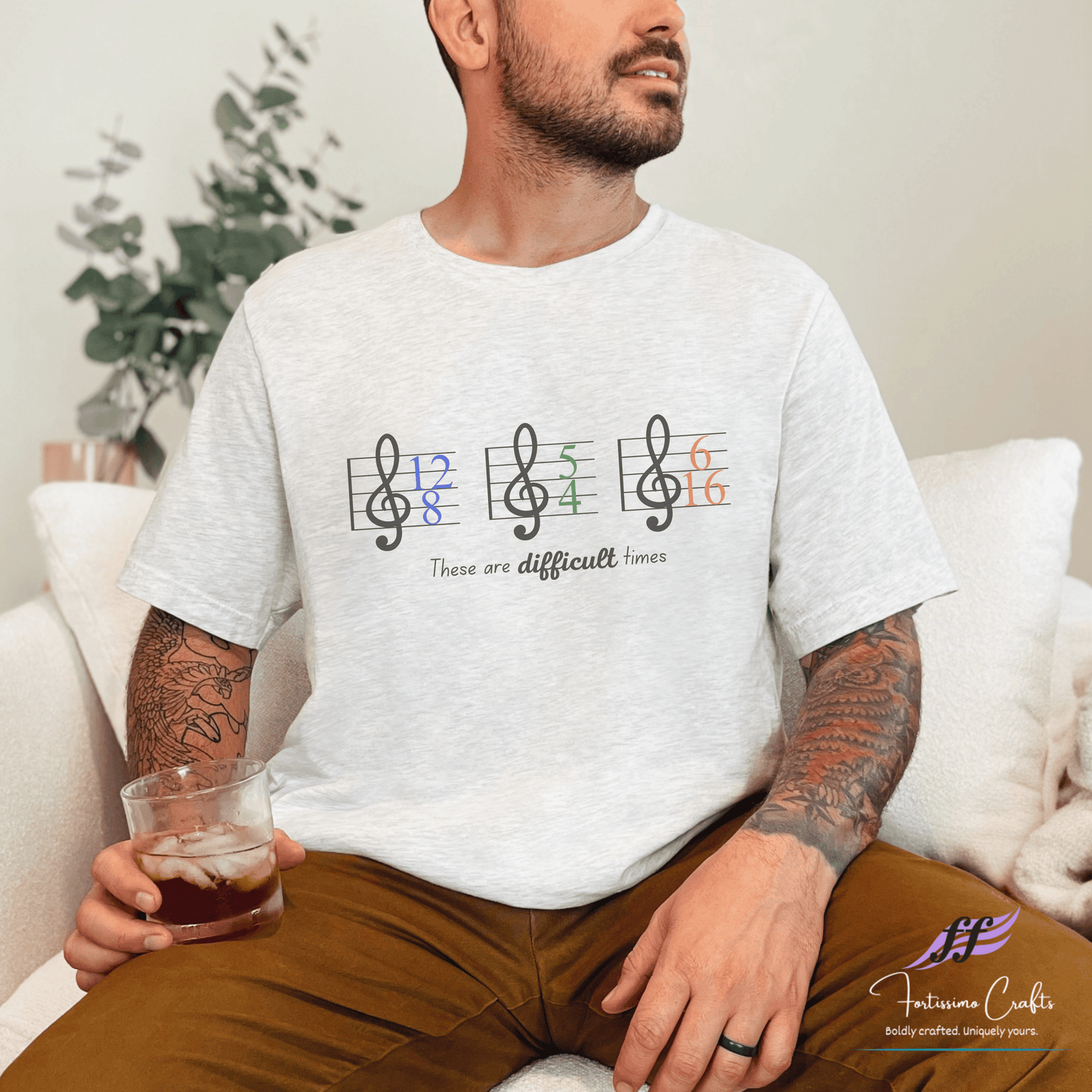 Man wearing a white t-shirt with musical note design and text, sitting on a couch.