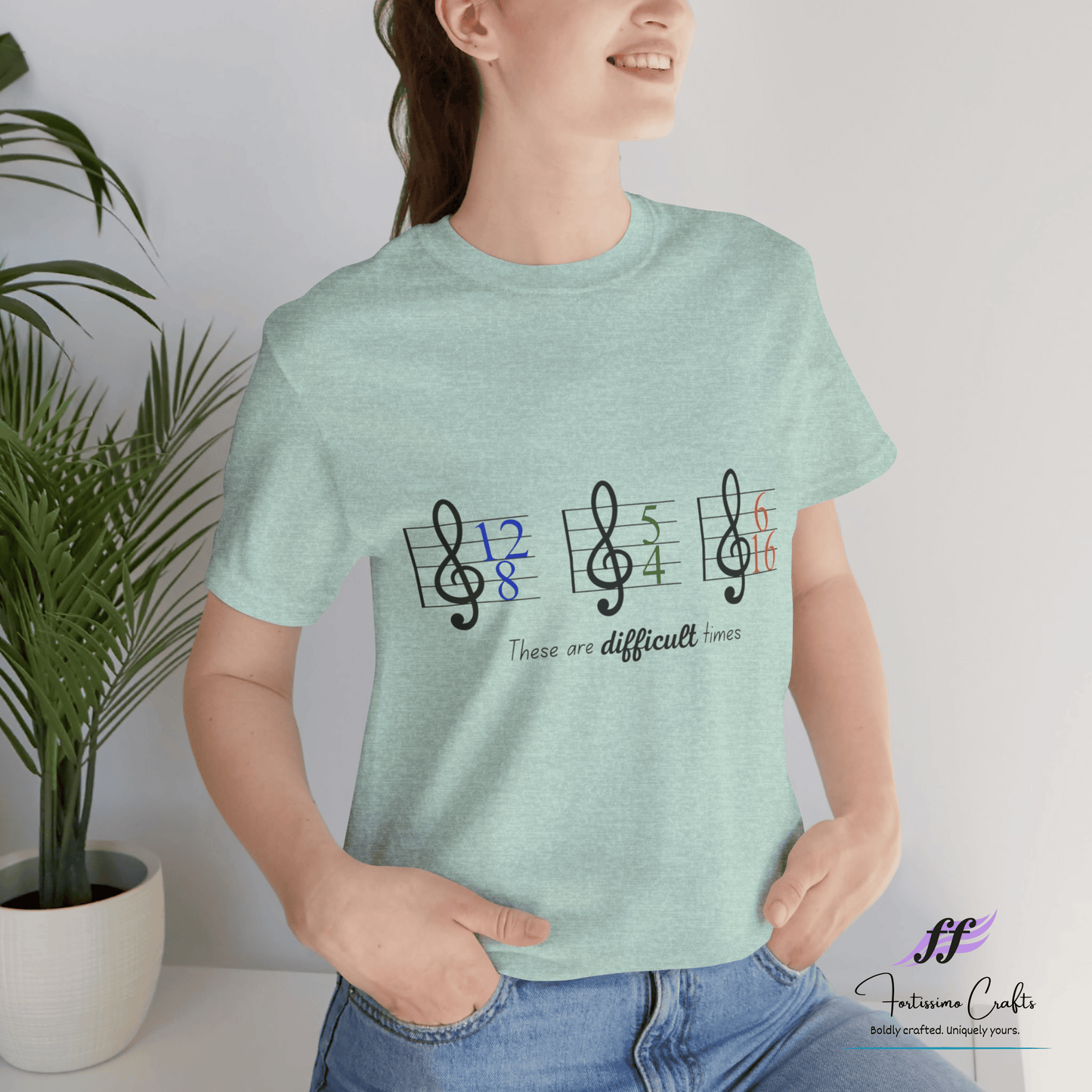 Person wearing a light green t-shirt with musical note design and text, standing indoors next to a plant.