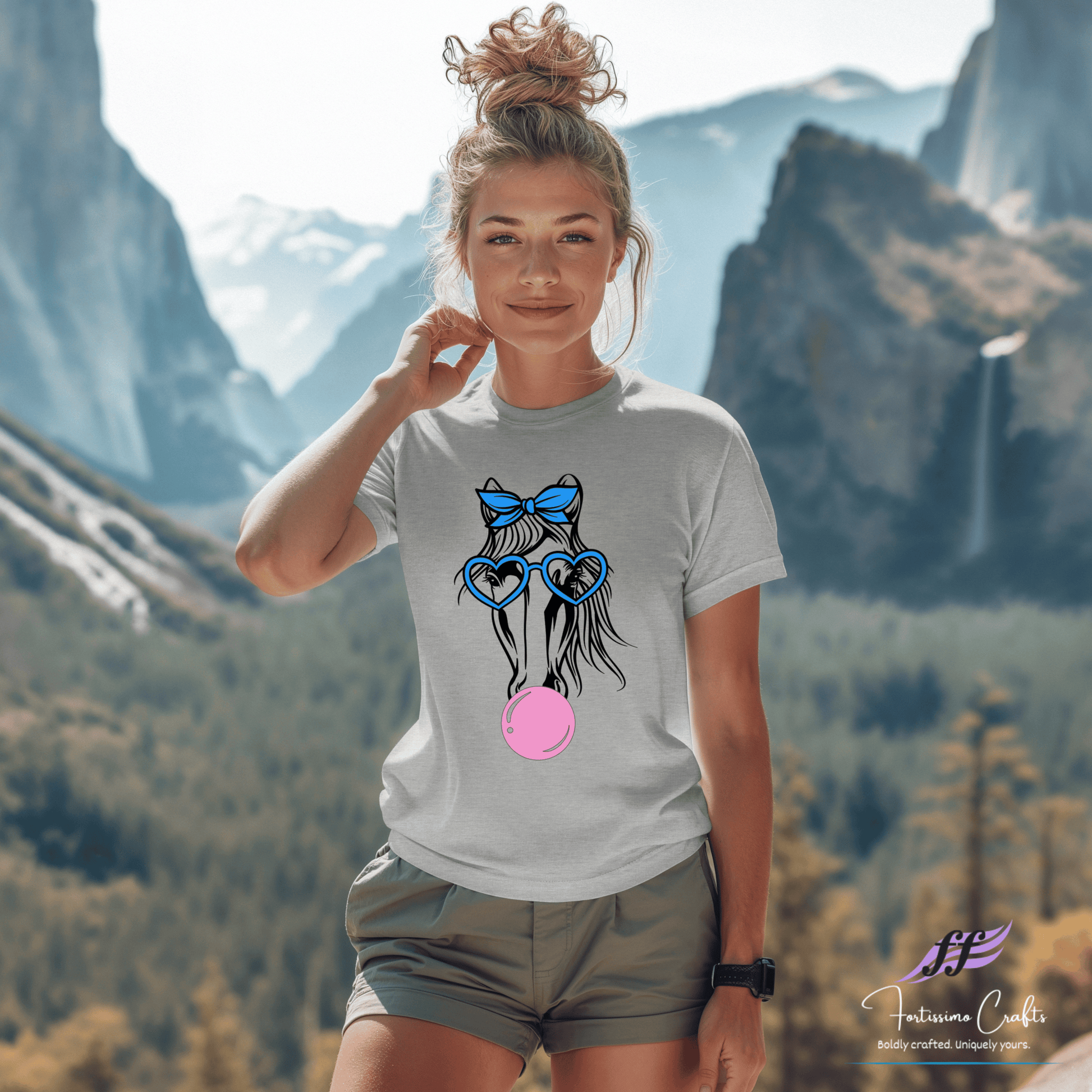 Woman wearing a t-shirt with a graphic design of a horse wearing glasses and a bow, standing in front of mountains.