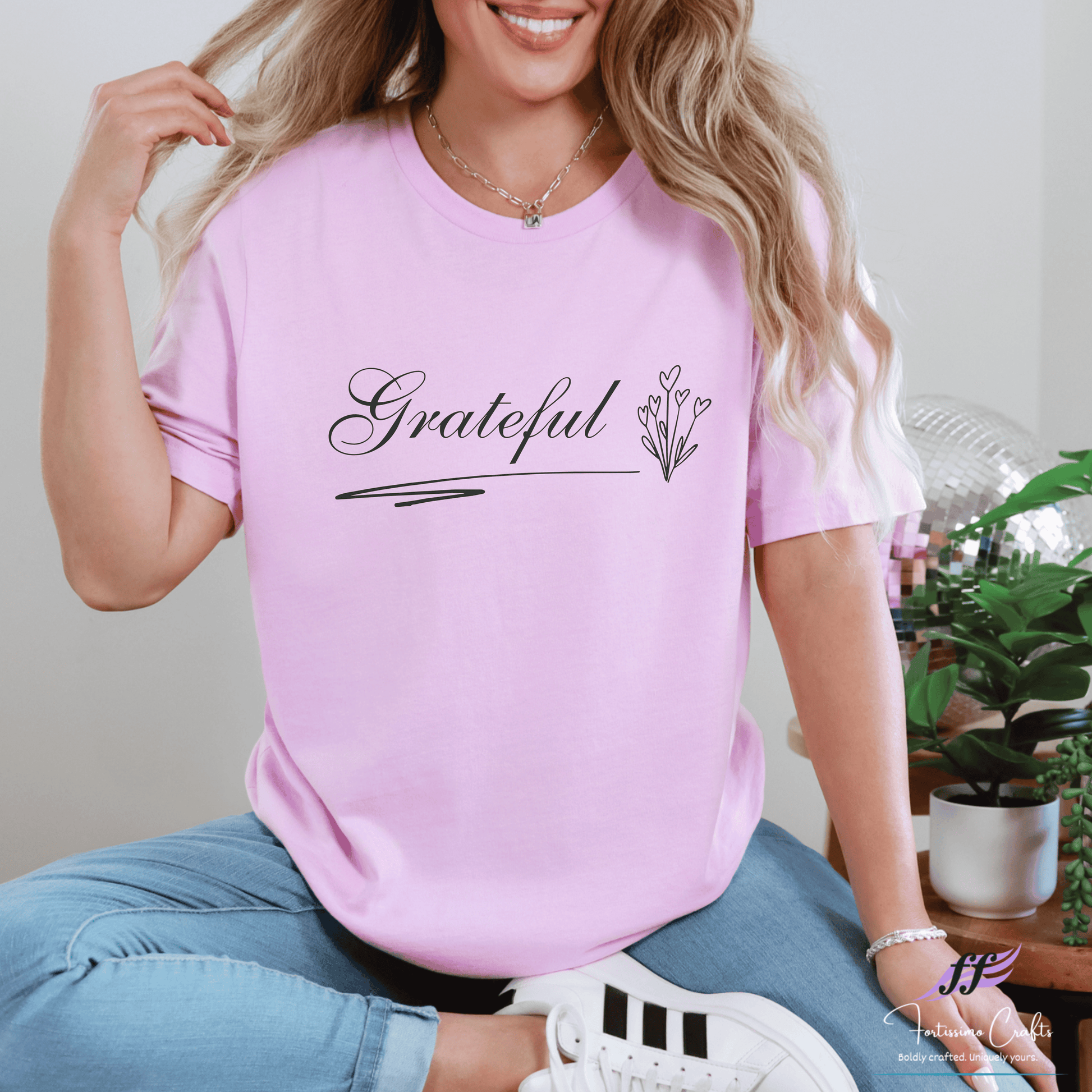 Woman wearing a pink t-shirt with 'Grateful' printed on it, sitting indoors.