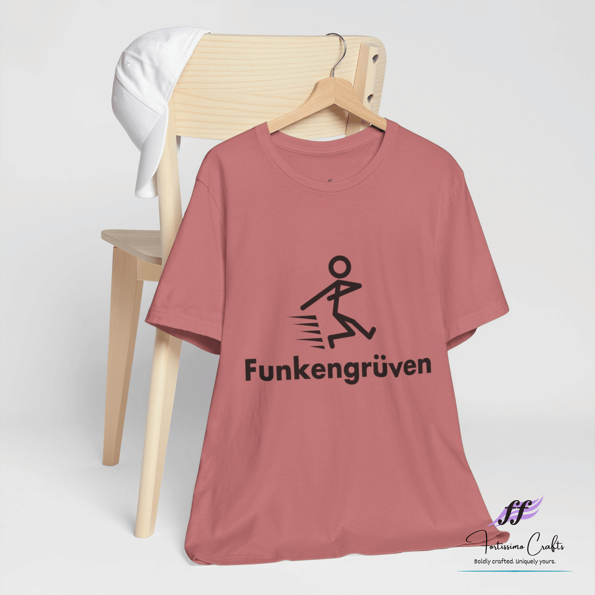 Pink t-shirt with 'Funkengörüven' design on a wooden chair against a white background