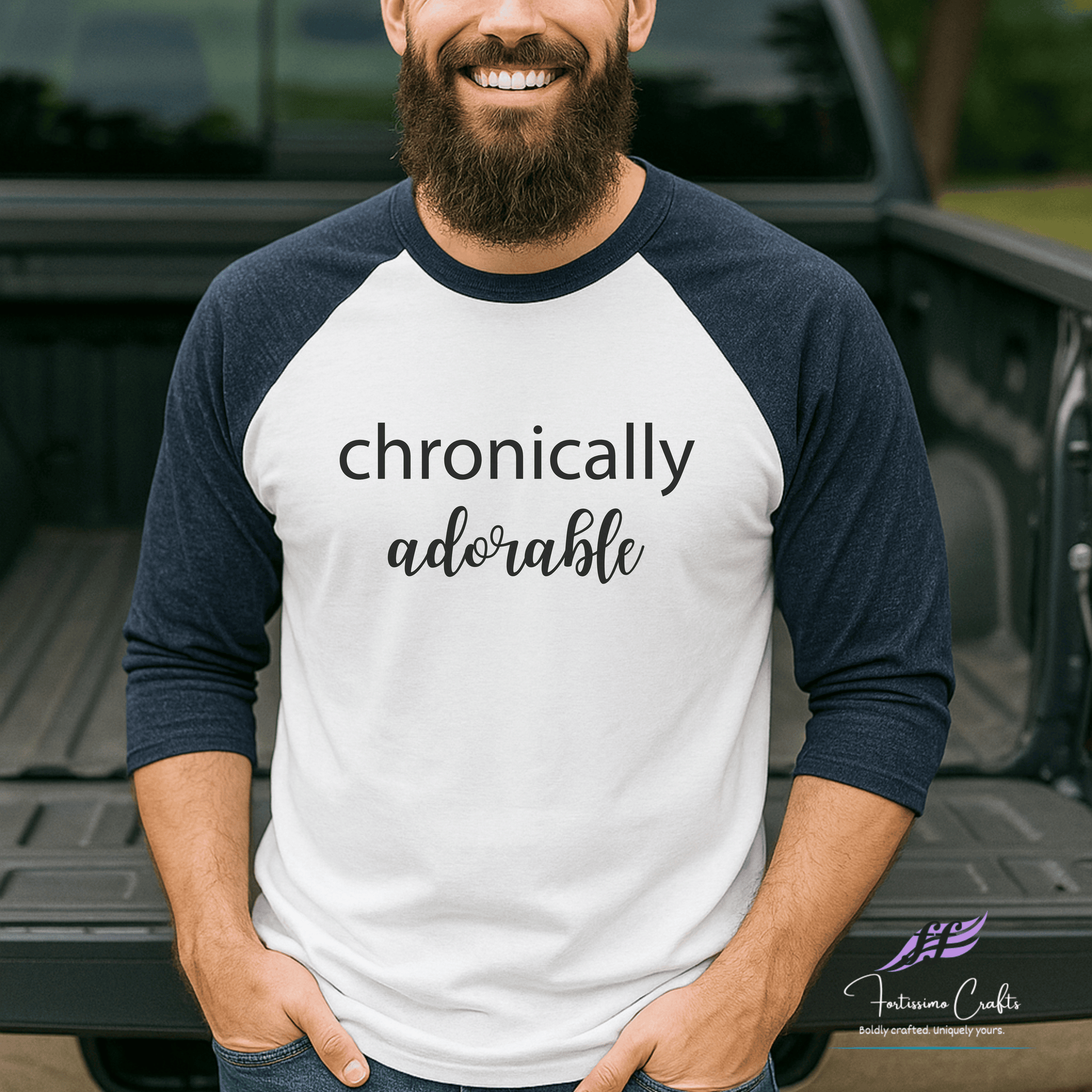 Man wearing a white and navy baseball shirt with 'chronically adorable' text, standing in front of a truck.