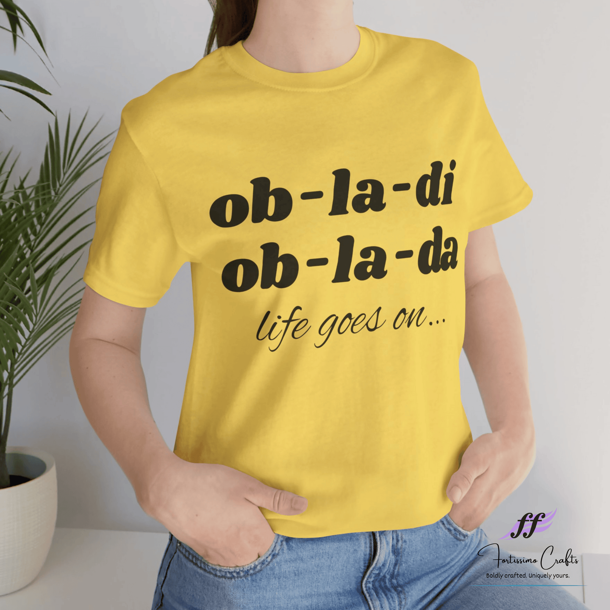 Yellow t-shirt with black text worn by a person, with a plant in the background