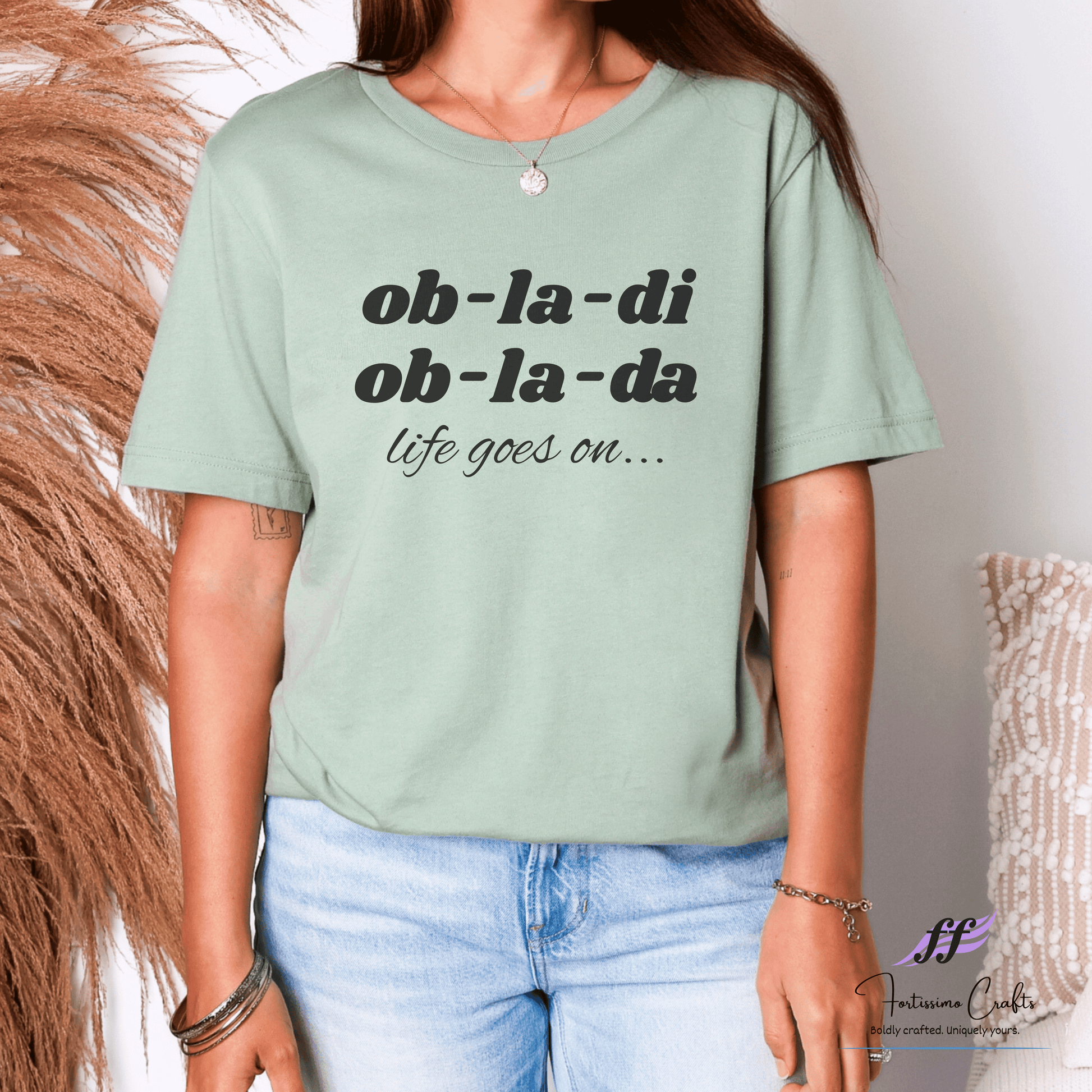 Person wearing a light green t-shirt with text and denim jeans against a neutral background