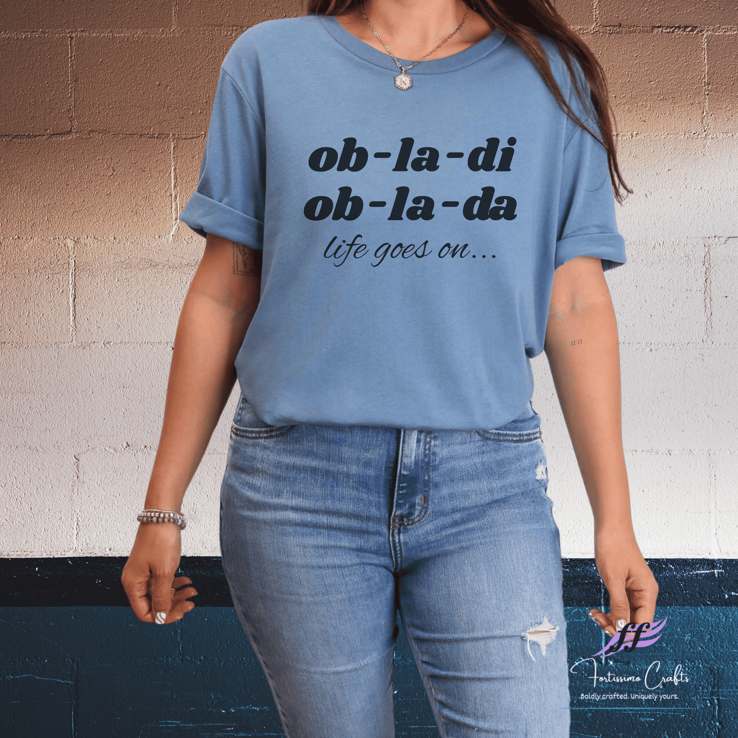 Person wearing a blue t-shirt with text and jeans against a wall.