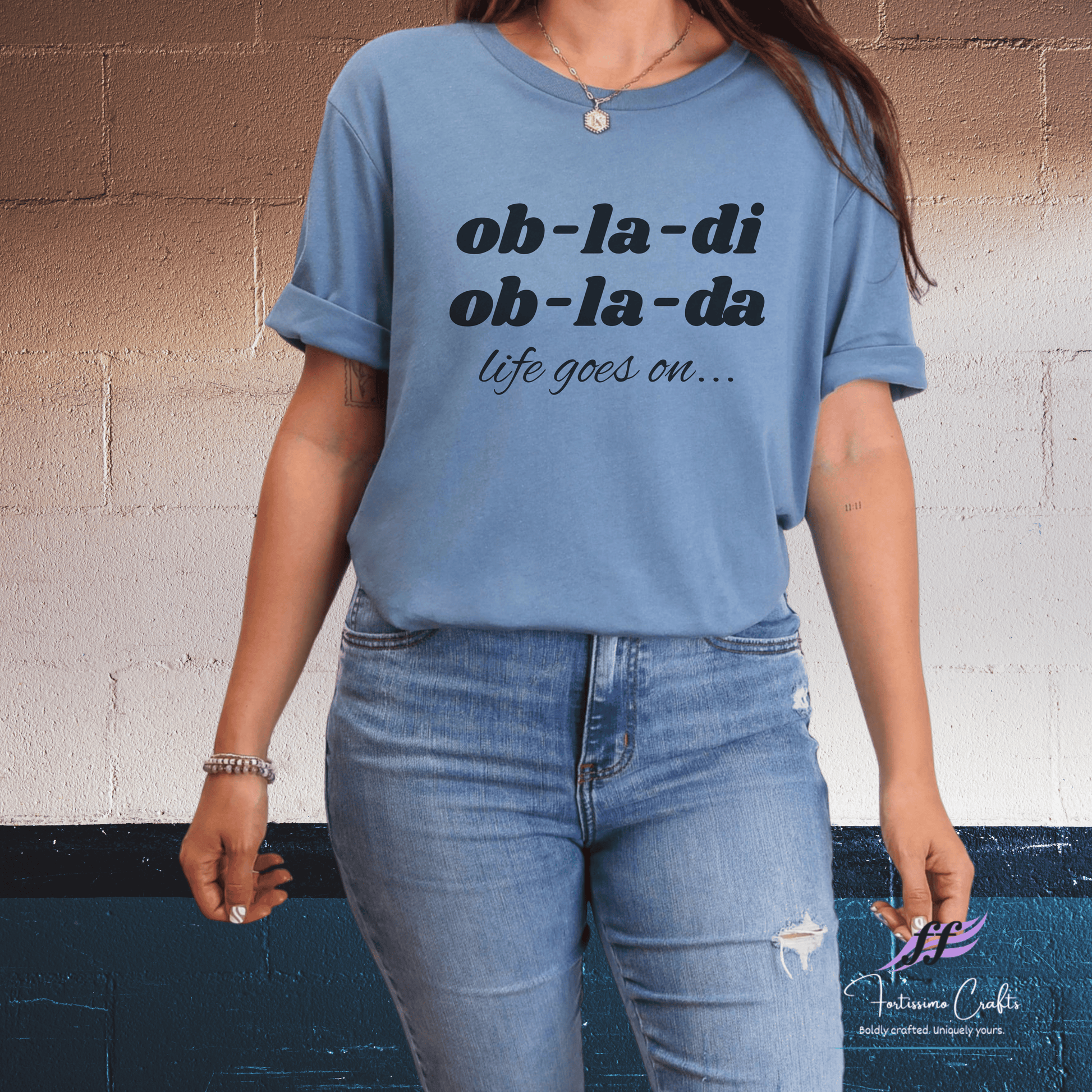 Person wearing a blue t-shirt with text and jeans against a wall.