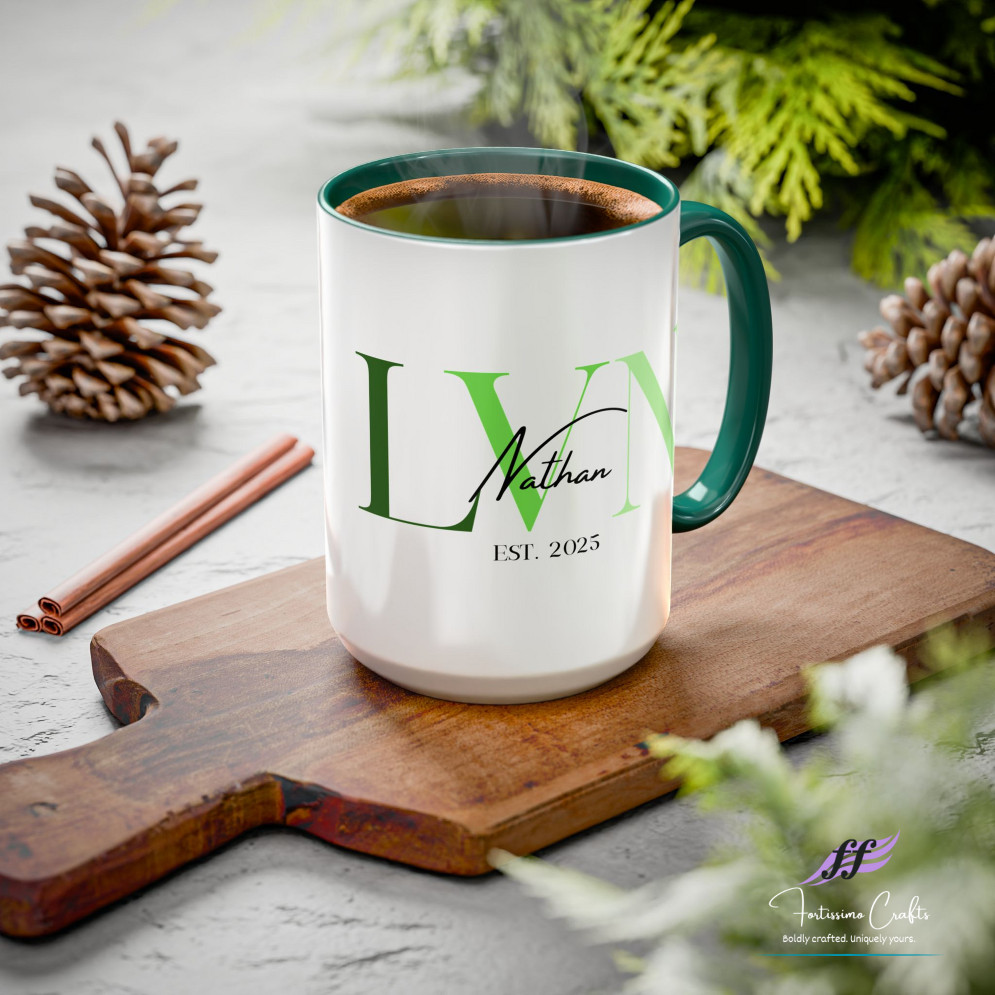 White mug with green interior and handle, featuring initials 'LV' and text, on a wooden board with pine cones and cinnamon sticks.