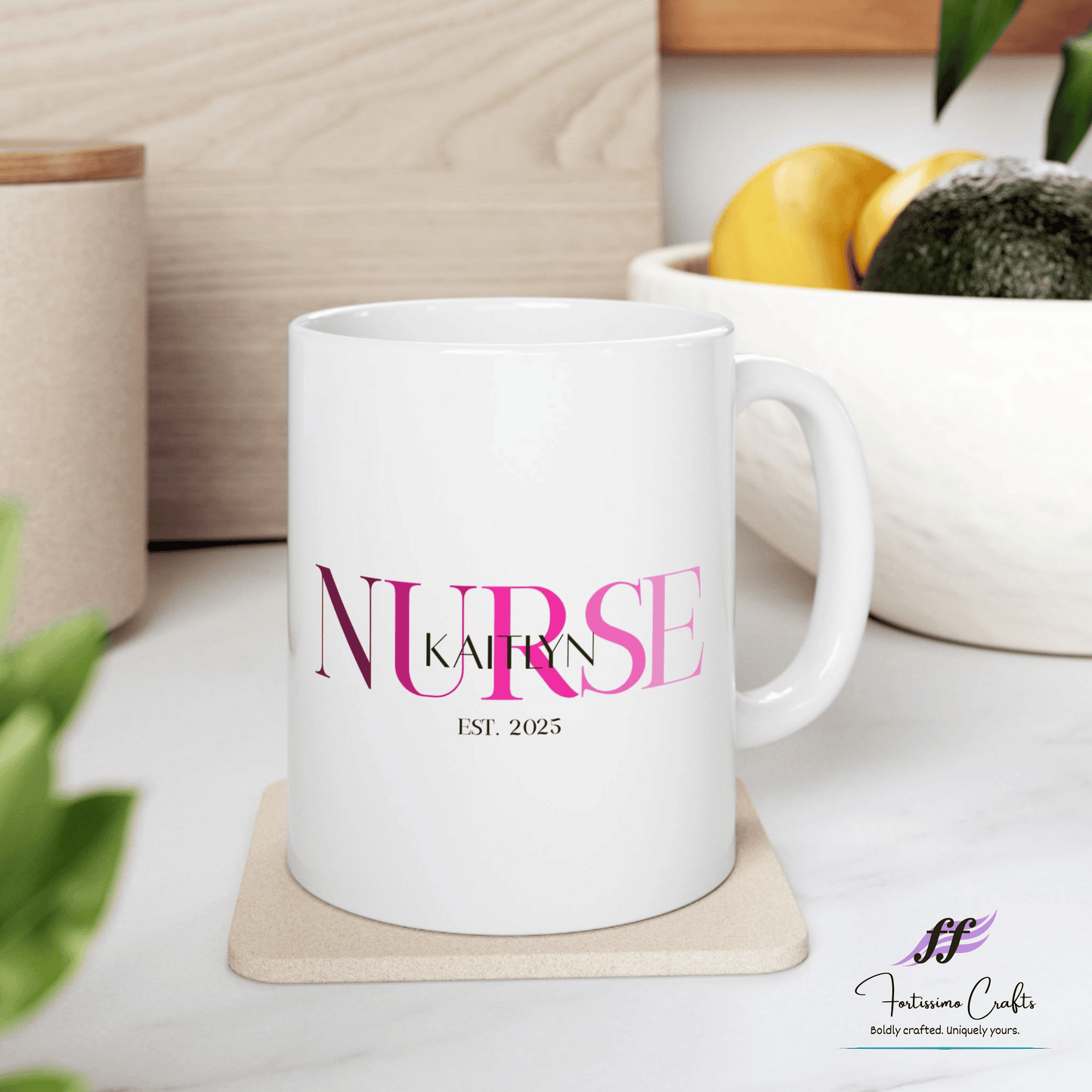 White ceramic mugs with NURSE in pink with the name Kaitlyn on top and est. 2025 underneath sitting on a table with a bowl of fruit in the background
