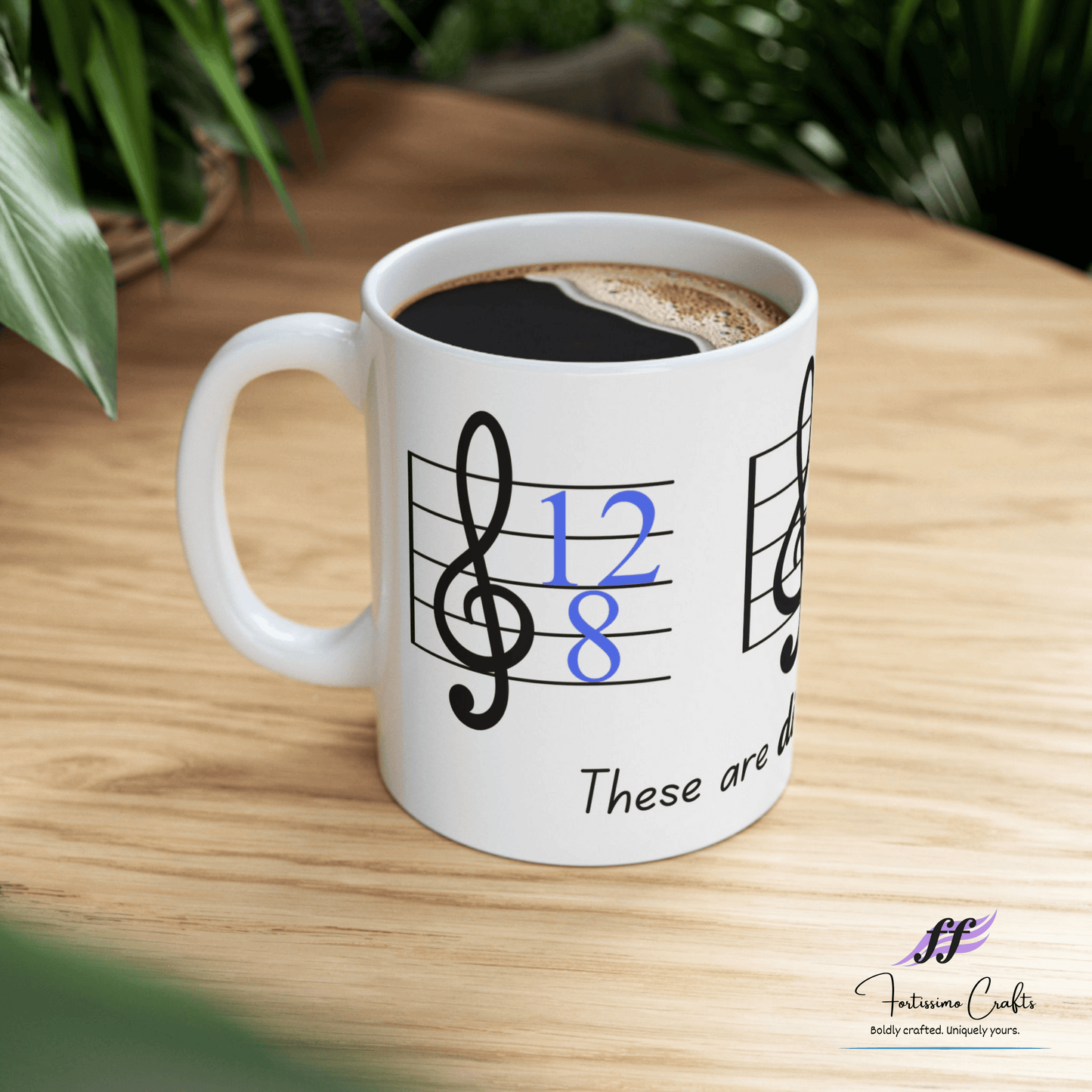 left view of 11oz white ceramic mug with music staff, 12/8 key signature and these are difficult times on a table with plants in the background