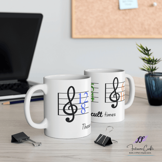 Two cups with music staff and these are difficult times on desk with laptop in the background