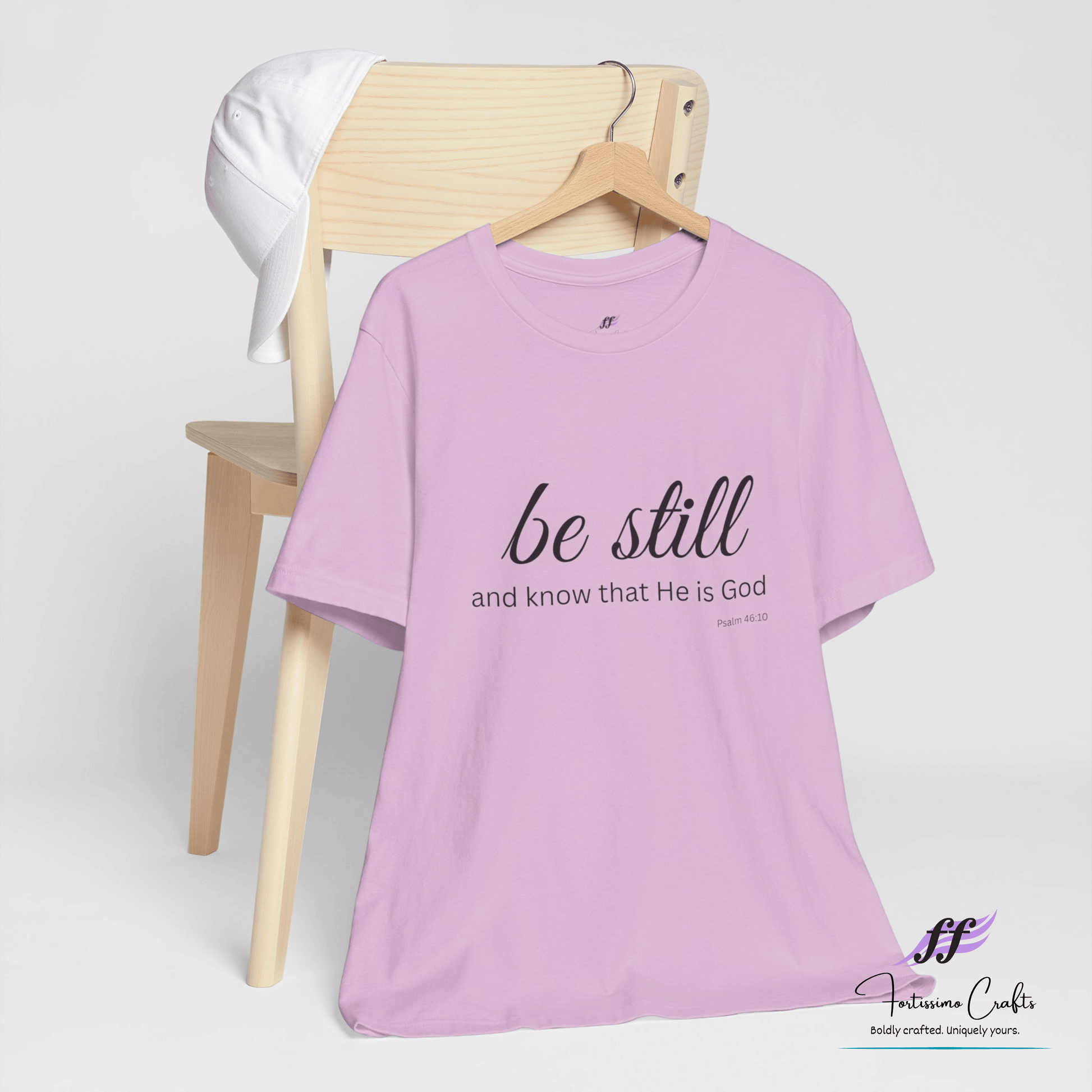 Purple t-shirt with 'be still and know that He is God' text on a wooden chair against a white background