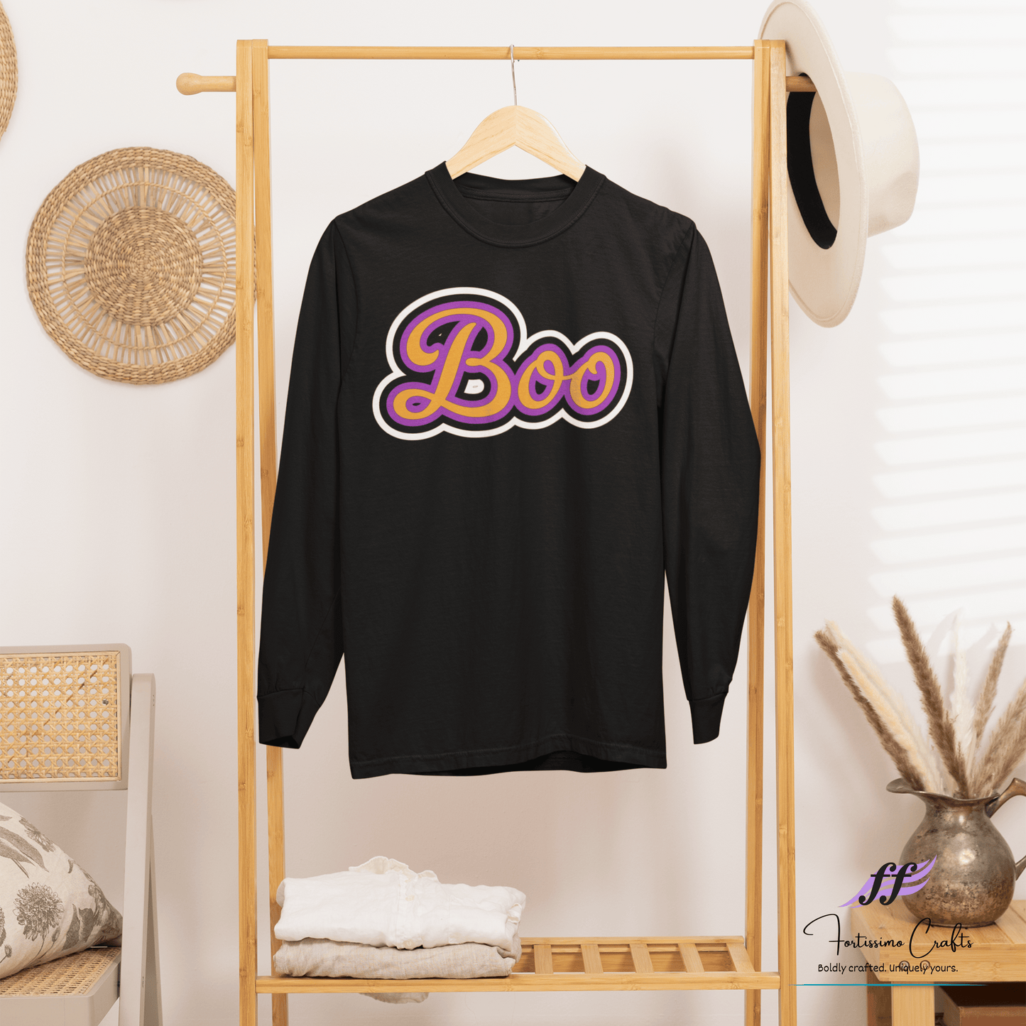 Black long-sleeve shirt with 'Boo' design hanging on a clothes rack in a boho setting with a white background.
