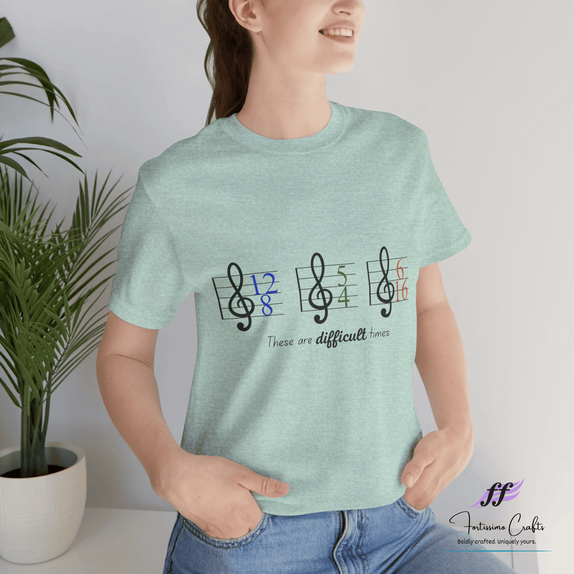 Person wearing a light green t-shirt with musical note design and text, standing indoors next to a plant.